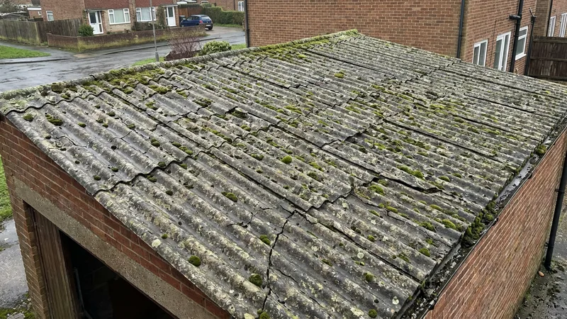 Weathered corrugated asbestos cement roof on a UK garage, showing moss growth and age deterioration